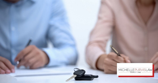Car keys on table with people and paperwork in background.