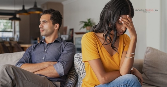 Couple sitting on couch, woman holding her head.