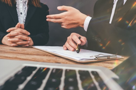 Two people sitting behind table with clipboard and pen.